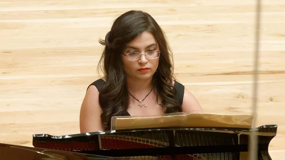 A women with dark hair, wearing a black dress, performing on the piano.